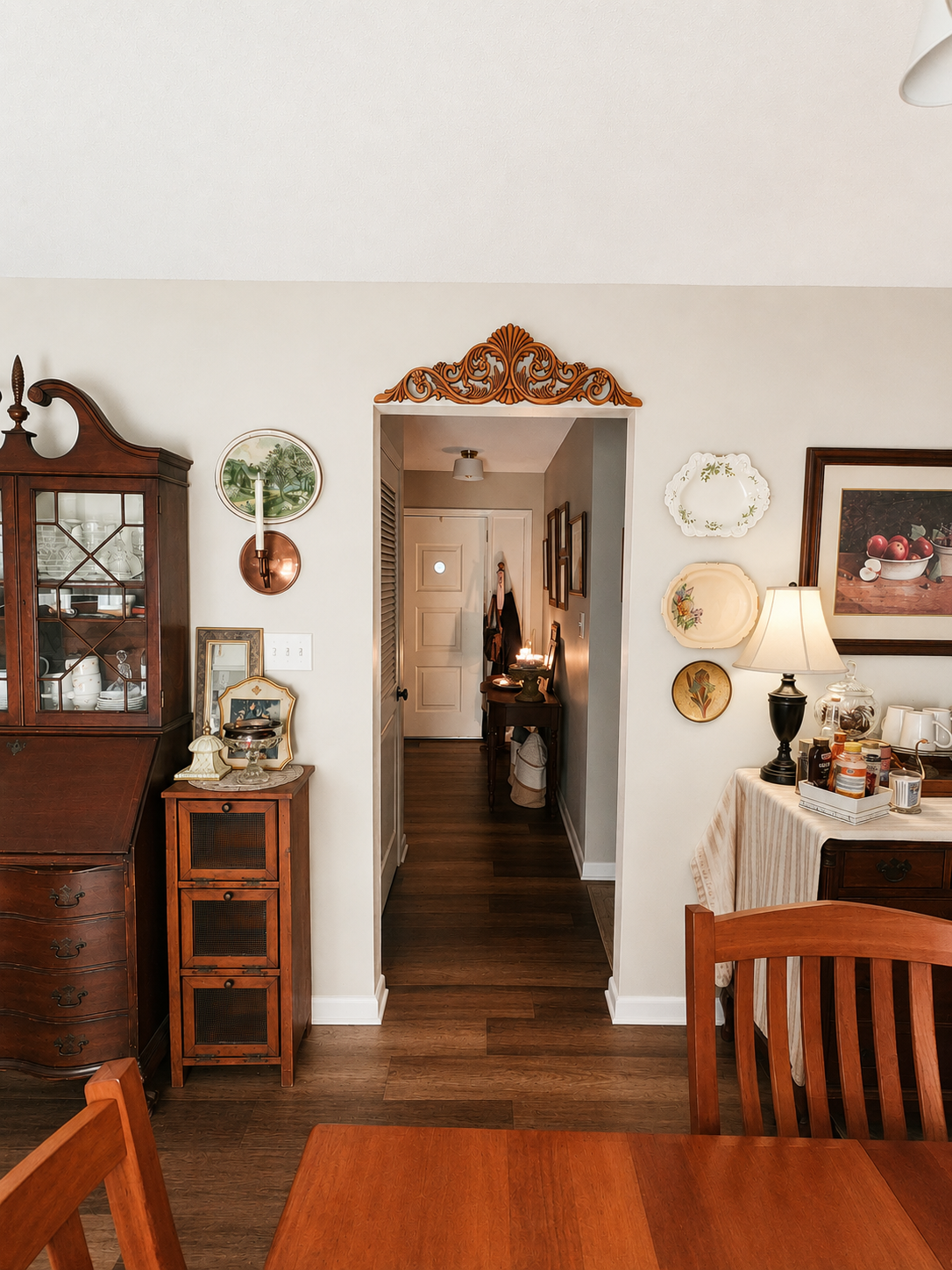 Dining room with ornate carved pediment over doorway, antique secretary desk, and plate wall display